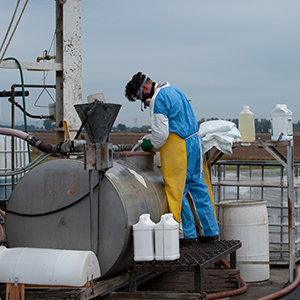 Pesticide Applicator in Personal Protective Equipment standing on a platform while mixing pesticides in a large tank