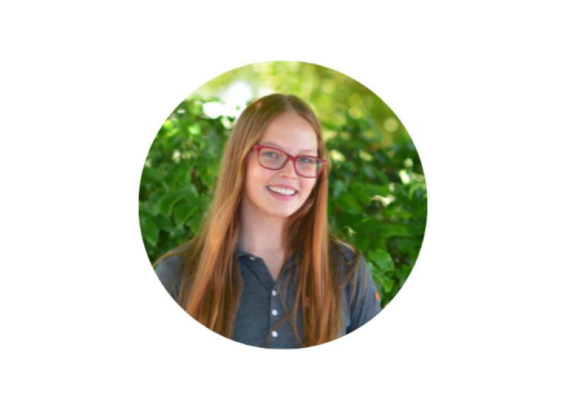 Undergraduate student Ali Merkle smiles slightly at the camera in front of lush green foliage